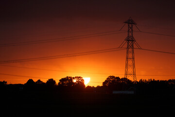 Vibrant sunset casting orange hues over landscape with silhouetted power lines and trees