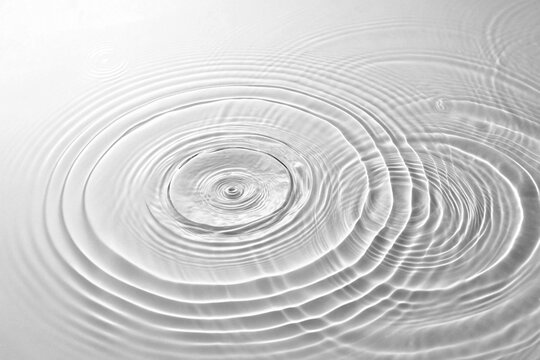 A serene and minimalist view of gentle concentric water waves expanding from two impact points, creating an elegant interference pattern on a clear surface.