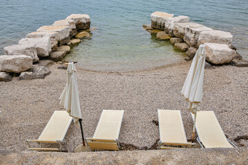 Beach loungers with umbrellas on pebble shore in Croatia.