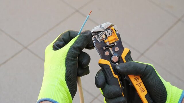 Man in safety gloves stripping insulation from cable with wire stripper, close up