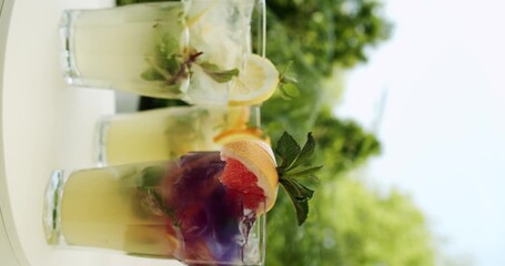 Refreshing summer soft lemonade drink with lemon, citrus, orange, grapefruit, mint, water and ice, glasses with lemonade rotating. Fresh lemonade with mint in glasses. Vertical video for stories.