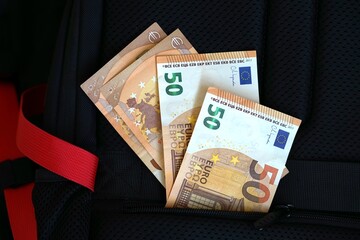 Fifty euro banknotes partially hidden in black backpack pocket. Concept of euro cash, personal finance and financial mobility, travel or savings