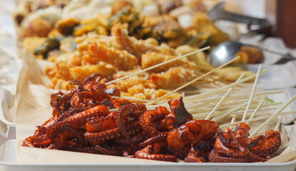 Appetizing grilled baby octopus skewers served at a vibrant food market, showcasing rich textures, seafood variety, and delicious street food culture in warm natural lighting.