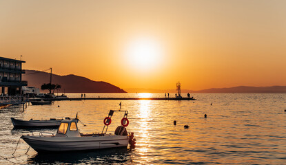 Small motorboats are gently rocking on the calm sea water near the pier during a picturesque golden sunset, creating a serene and peaceful atmosphere