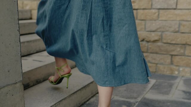 Close-up of a woman wearing a denim skirt and green heels, walking up concrete stairs outdoors. Woman in Denim Skirt and Green Heels Walking Up Concrete Stairs Outdoors