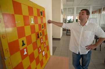 Caucasian man standing at wall mounted magnetic chessboard demonstration. 