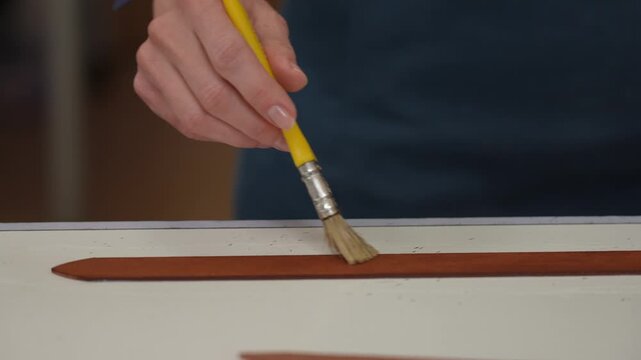 A craftsman uses a brush to cover leather parts. 