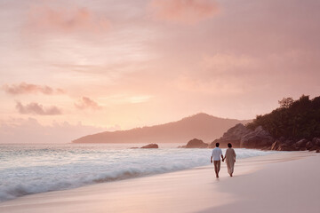Romantic beach escape at sunset. A couple strolls handinhand along a pristine beach, bathed in the warm light of dusk. Ideal for travel, love, or honeymoon concepts.