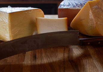 Various types of cheese with large dark-bladed cheese knife in foreground and different cheese...