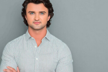 Obraz premium Confident young man in striped shirt posing with arms crossed against gray studio background