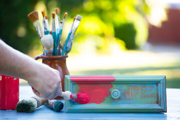 Woman painting a wooden furniture outdoors, an eco-friendly re-use business.