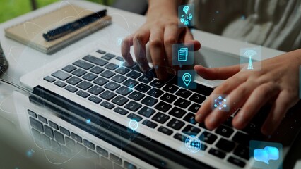 A close-up view of hands typing on a laptop keyboard showcasing digital icons that symbolize technology and communication, illustrating a modern workspace environment. Xenic