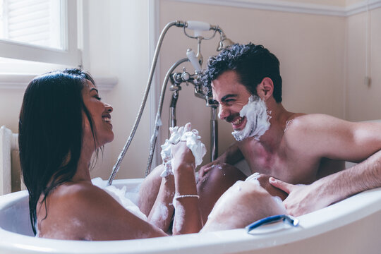 Young multi-ethnic couple enjoying a playful bath together, laughing and having fun while playfully tossing shaving cream at each other, creating a joyful and intimate atmosphere - Powered by Adobe