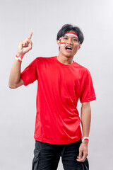 Excited young Indonesian man in red shirt with face paint raises one finger, expressing pride and...