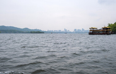 Traditional boat on West Lake, Hangzhou City skyline background, China. Rainy day