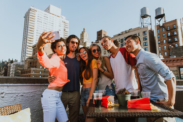 Cheerful young multi-ethnic friends toasting drinks while enjoying a vibrant rooftop party in new york city, surrounded by delicious food, laughter, and the stunning skyline