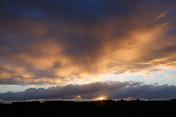 Dramatic sunset over the horizon with colorful clouds illuminating the sky near a nature reserve in the evening