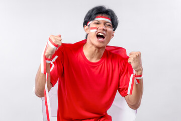 Excited young Indonesian man celebrates Independence Day with pride, wearing red and white, raising...