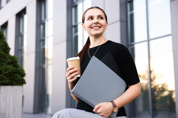 Successful businesswoman with coffee and folder near office building