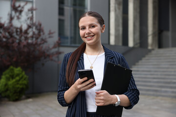 Happy businesswoman with smartphone near office building