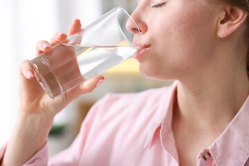 Young woman drinking water from glass at home, closeup