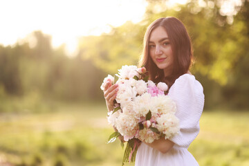 Fototapeta premium Beautiful woman with bouquet of peonies in park on sunny day. Space for text