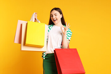 Excited woman with shopping bags showing okay gesture on yellow background