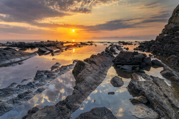 Sunset over the sea with rocks in the foreground and calm waves, creating a scenic seascape.