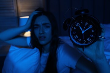 Frustrated woman with pillow and alarm clock suffering from insomnia at home, selective focus