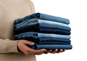 Person wearing a beige sweater holding a neat stack of folded blue denim jeans isolated on transparent background