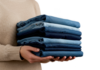 Person wearing a beige sweater holding a neat stack of folded blue denim jeans isolated on transparent background
