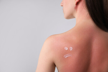 Woman with sun protection product on her sunburned skin against grey background, closeup. Space for...