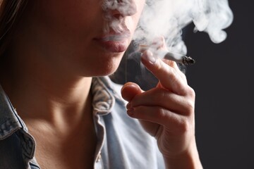 Fototapeta premium Woman in shirt smoking cigarette on dark background, closeup. Bad habit