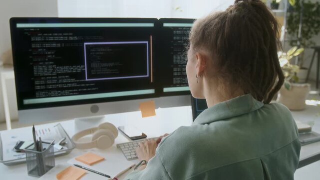 Unrecognizable female programmer focused on typing codes while working in IT office. She sitting at desk with office supplies and digital devices