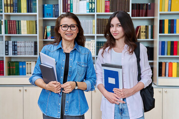 Portrait of teenage girl student with female teacher mentor looking at camera in library
