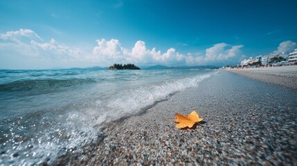 Yellow Autumn Leaf on a Pebble Beach Shoreline With Gentle Waves and Blue Sky, Symbolic Scene of Seasonal Change and Tranquility