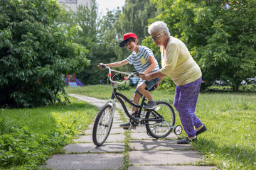Fototapeta premium Grandmother teaching grandson to ride bicycle in park - family bonding, cycling lessons, intergenerational activity, outdoor recreation. 