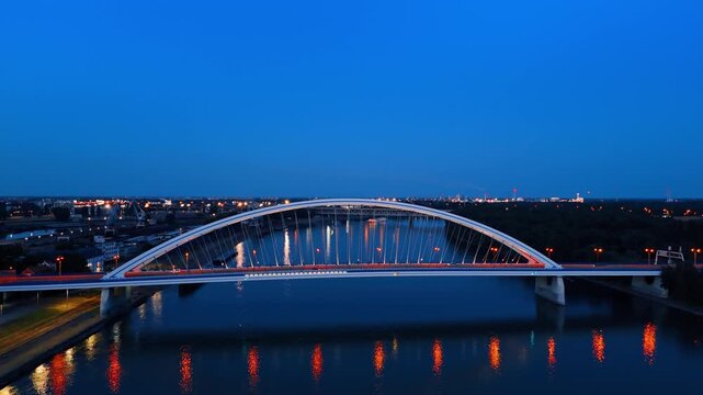 Lights from the Appolo Bridge reflect in the waterscape of the Danube. Drone rising revealing view on Bratislava at dusk time.