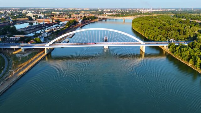 Flight over the blue waterscape of the Danube. Footage at the beautiful Appolo Bridge with a riverboat passing under. Bratislava, Slovakia.