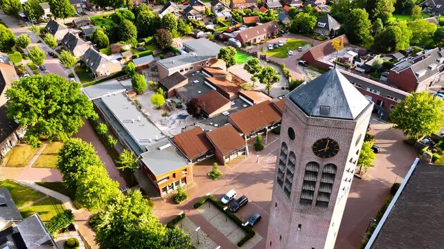 Flight around the hexagon clock tower freestanding near the Saint Lawrence Church. Lovely panorama of Vierlingsbeek, Netherlands at backdrop.