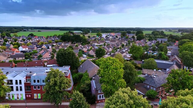 Flight over green trees approaching the similar residential houses. Lovely town of Vierlingsbeek, Netherlands on cloudy day.