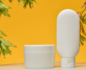 Cosmetic products without labels tube, flat round jar, stand on white table against bright yellow background