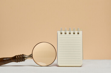 An open notebook with blank lined sheets of paper and a magnifying glass next to it. Searching for information, planning, analyzing or studying.
