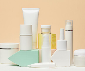 White plastic jars and tubes for cosmetics, gels, creams and tones on a beige background