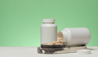 Two white plastic jars, one of which is overturned and capsules are spilling out, are placed on a marble stand.