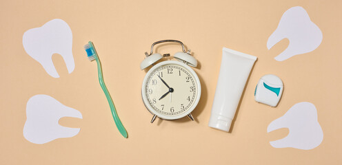Oral hygiene set including toothbrush, toothpaste and dental floss, alarm clock, on beige background.