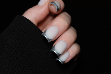 Stylish woman’s hand with silver French tips in black sleeves. Contrasting textures and tones...
