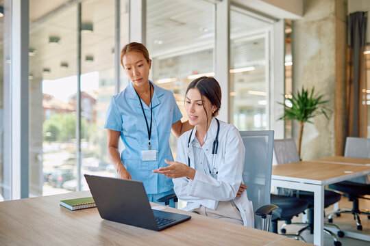 Doctor and nurse reviewing patient information on laptop, working together in modern hospital setting