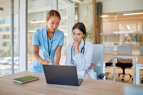 Female doctor and nurse are using laptop and discussing about diagnosis in bright modern hospital meeting room - Powered by Adobe