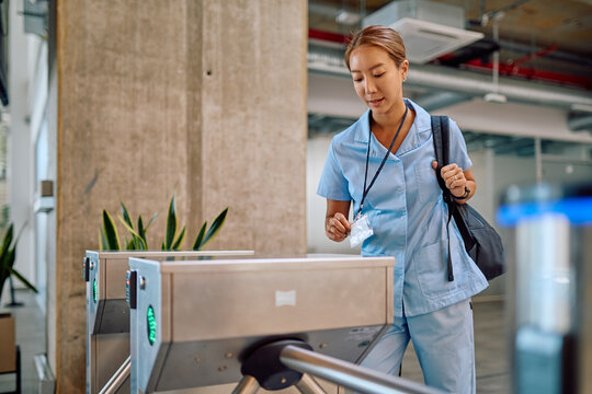 Asian female doctor in blue uniform using her electronic badge to open automatic turnstile gate and enter restricted area in modern hospital - Powered by Adobe